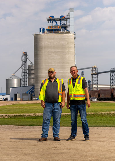 Two men standing in front of a grain elevator.