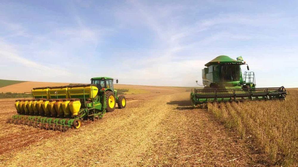 A planter and combine harvester moving in opposite directions through a field in Brazil