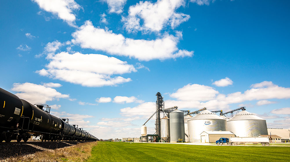 Grain bins beside a railroad track under a cloudy blue sky.
