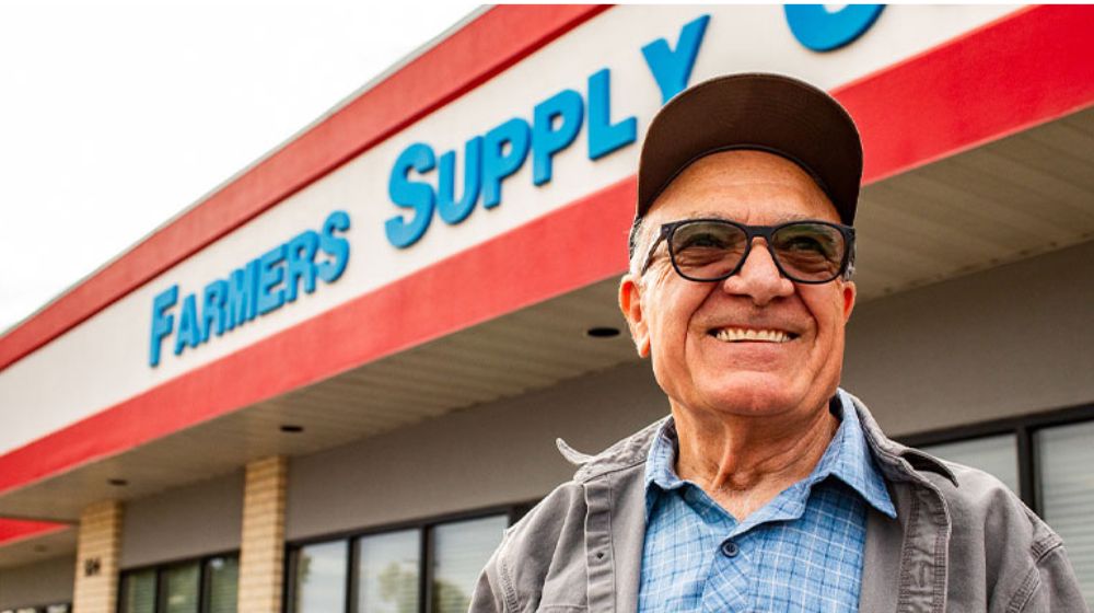 Man standing in front of building that says Farmers Supply Cooperative on the outside