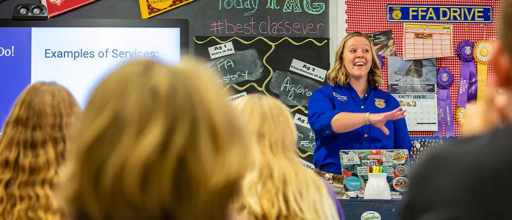 A teacher in front of a classroom gesturing to students