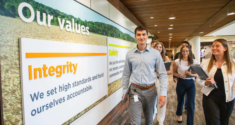 Group of interns walk down an office hallway beside a wall display highlighting CHS values, including integrity and safety