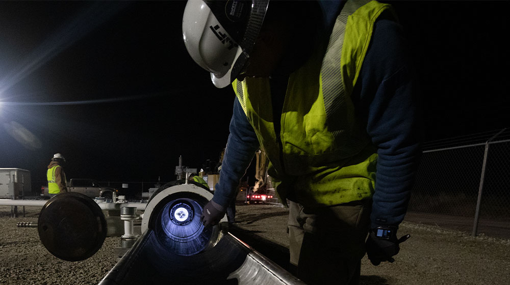Man wearing yellow safety vest and hard hat checking a pipeline that contains a smart pipeline inspection gauge at night.