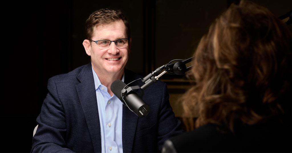 Nelson Neale speaking into a microphone across the table from host Malissa Fritz