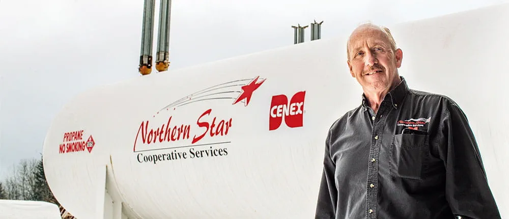 alt="Man standing next to bulk propane tank branded with Northern Star Cooperative Services and Cenex logos"