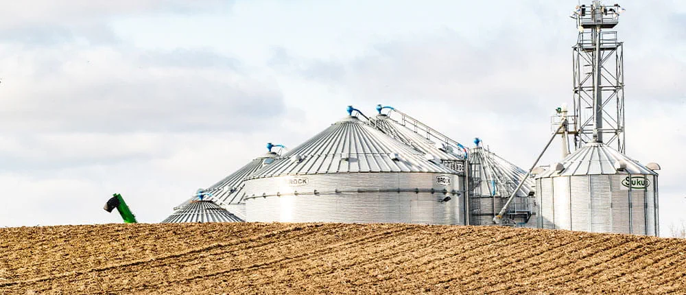 Grain bins in the background and harvested field in the foreground, under partly cloudy sky