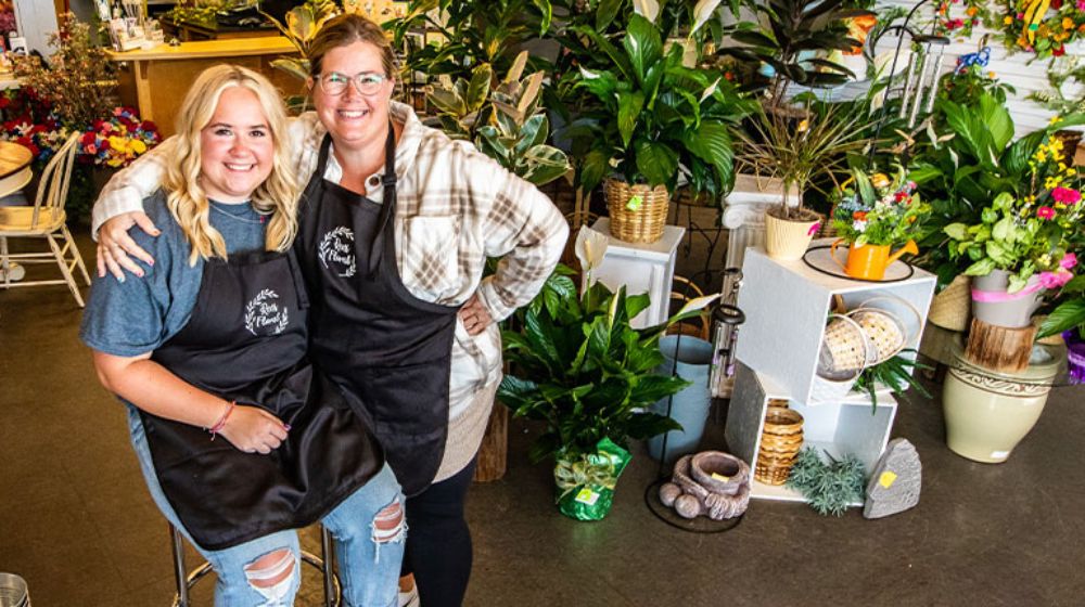 Two women standing next to each other in a flower shop.