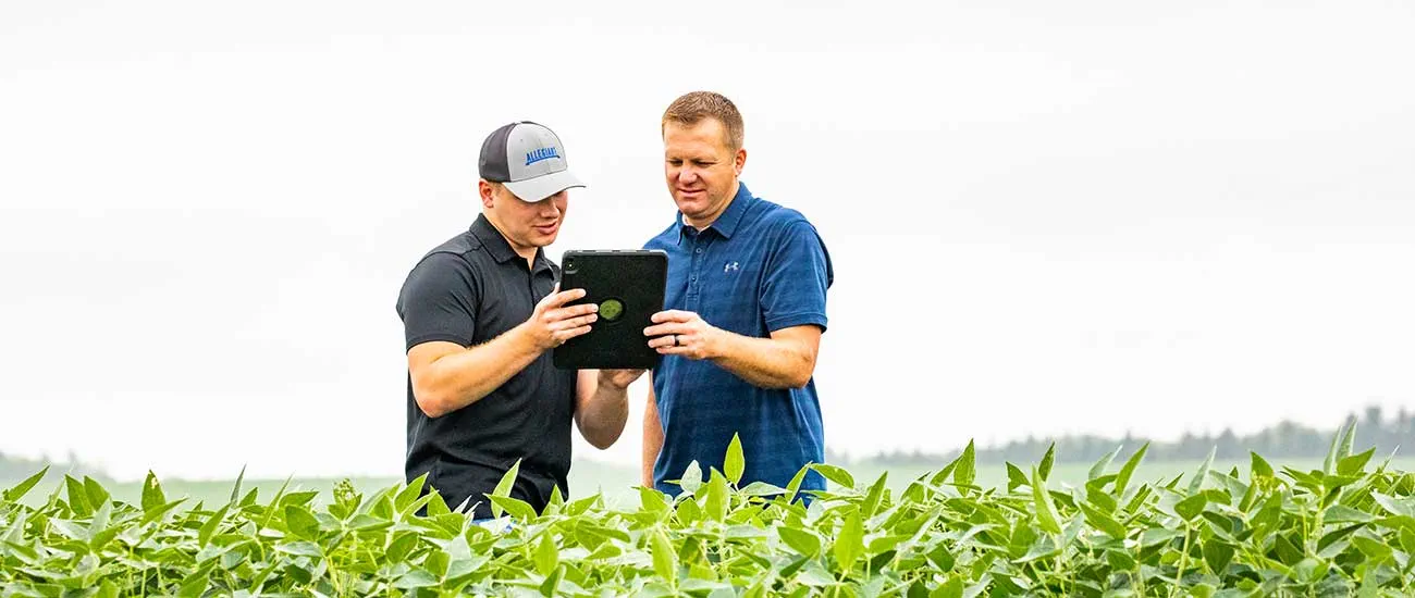 Two men standing in a field looking at a tablet