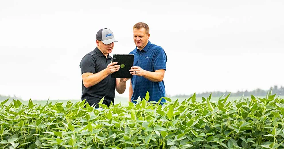 Two men standing in a field looking at a tablet.