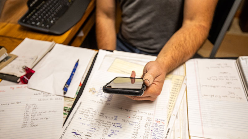 Person holding a phone while sitting at a desk with papers on it.