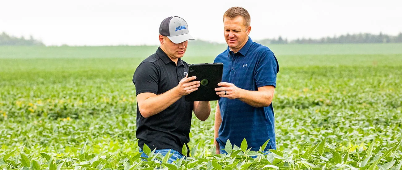 two men in field looking at ipad