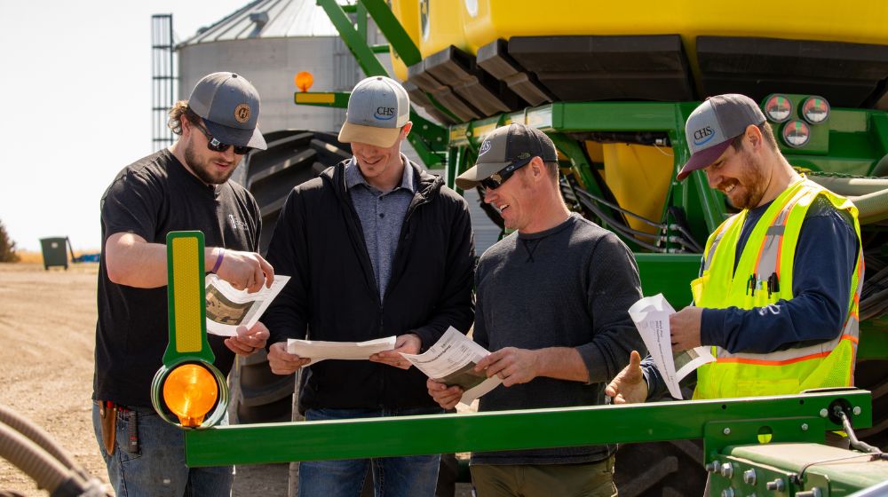 Four men standing beside farm equipment talking and smiling